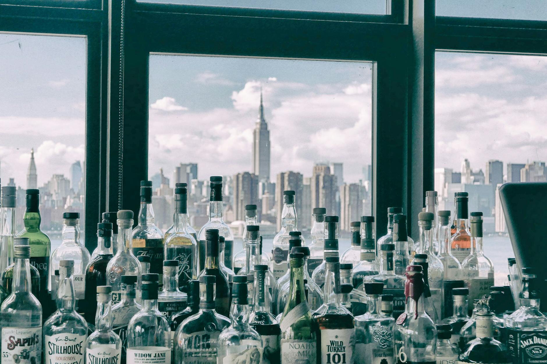 Botellas de bebidas alcohólicas almacenadas con vista urbana desde el interior de un bar
